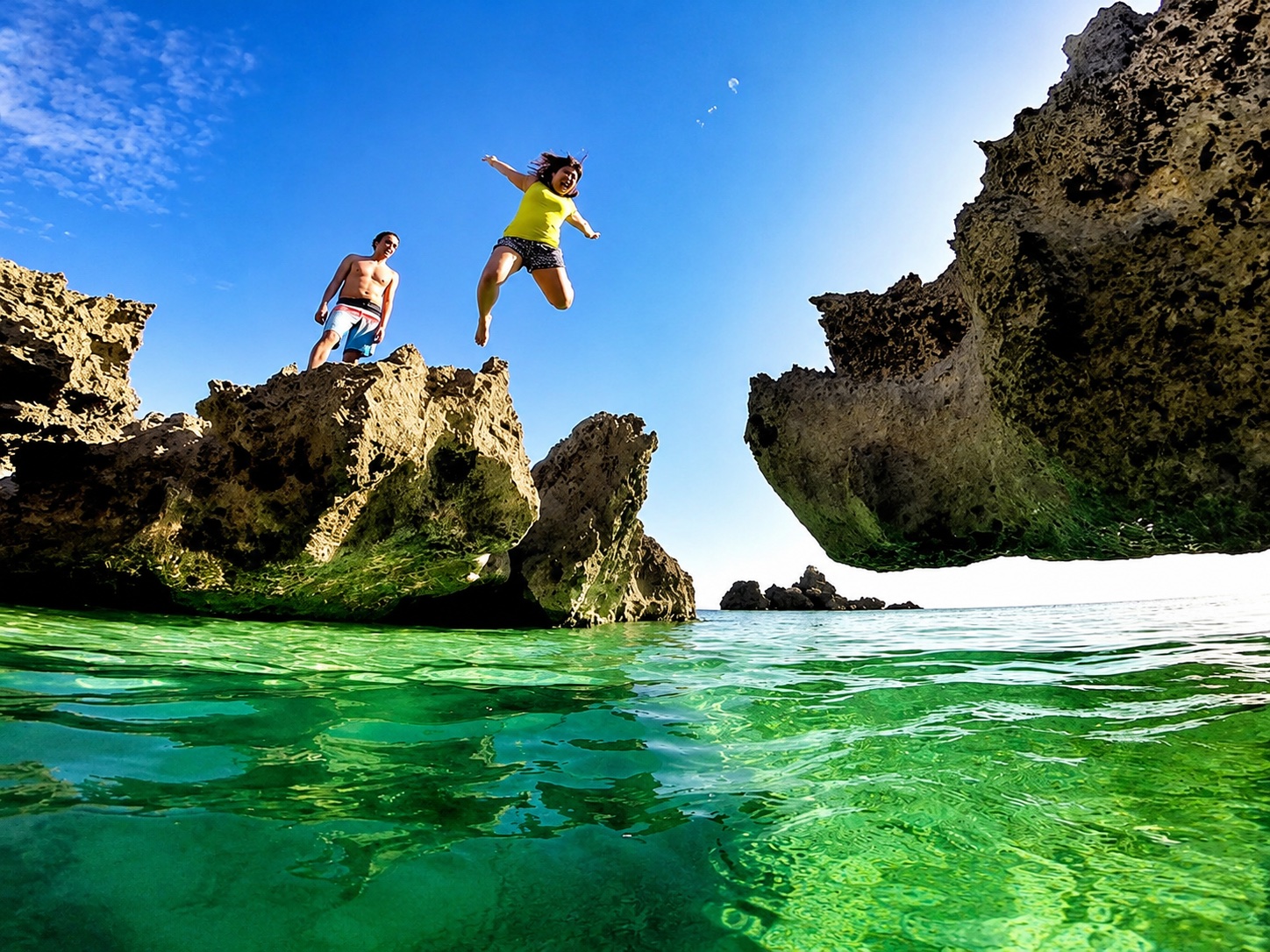 Friend mid-air leaping off a cliff into turquoise water